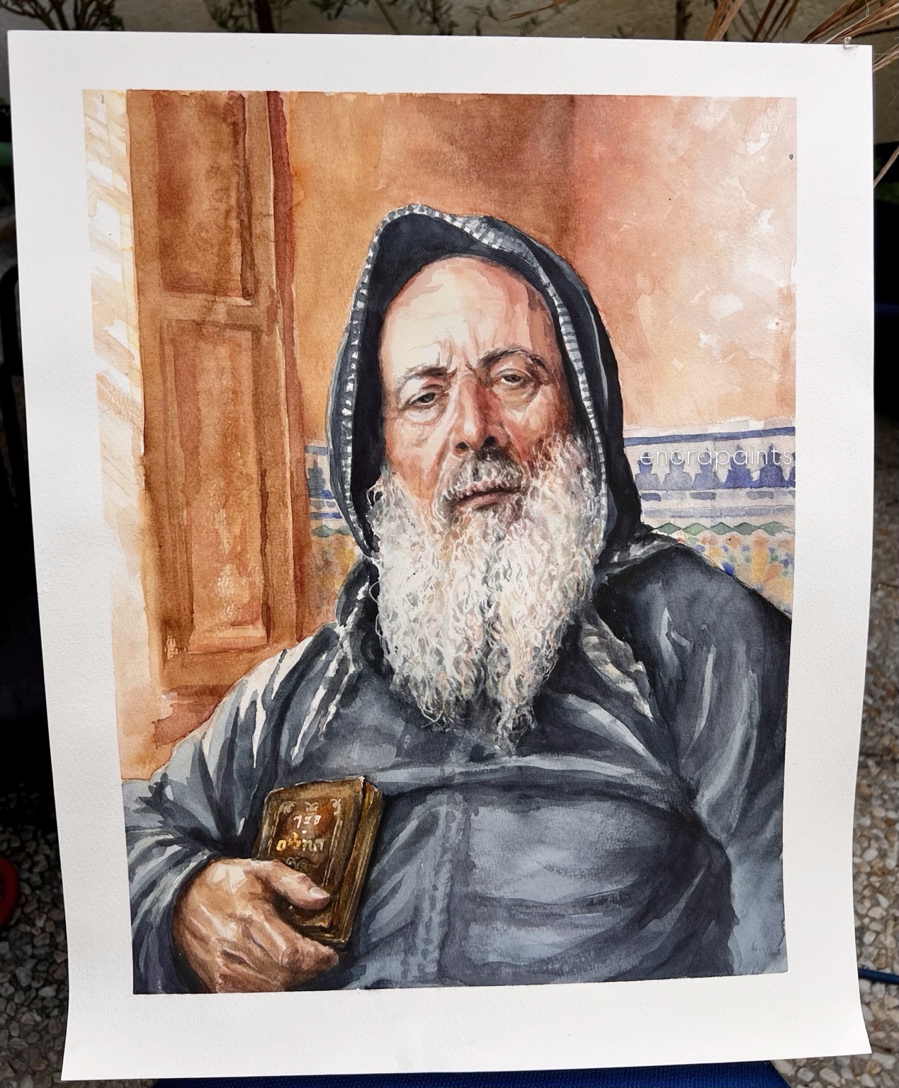 Watercolor portrait of a bearded man in a dark hooded robe holding a small book, Essaouira